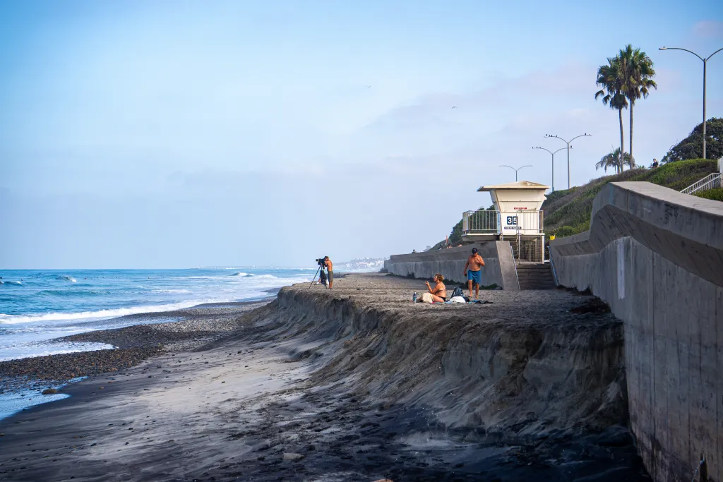 Erosion of Tamarack State Beach in Carlsbad, California, with exposed sand cliffs and waves crashing near the shore.