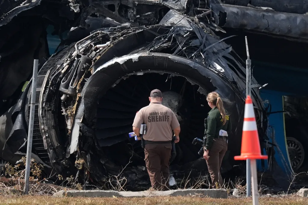 Law enforcement officers inspect the destroyed engine of an Amazon cargo plane after it overran a runway.