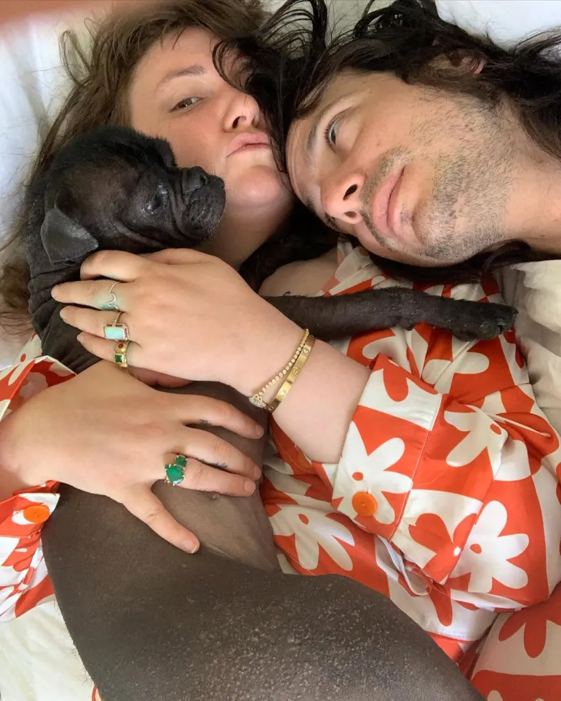 Lena Dunham, her husband Luis, and a small black hairless dog lie in bed together.
