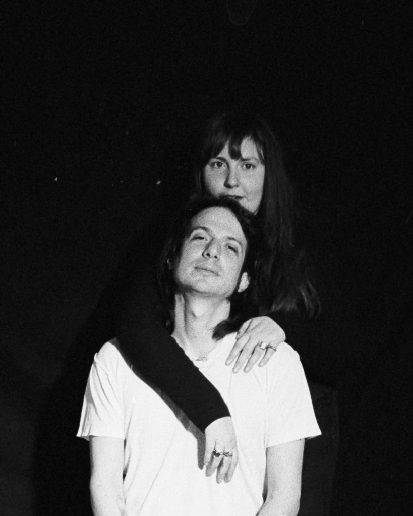 Black and white photo of Lena Dunham embracing her husband, Luis Felber, from behind.
