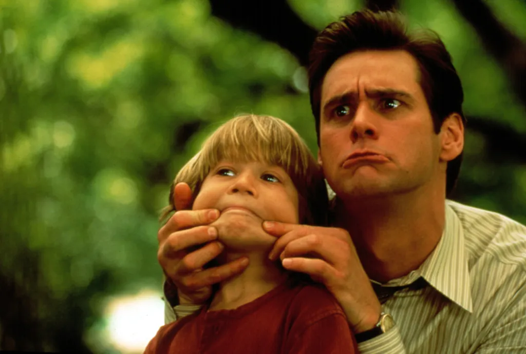 Jim Carrey making a funny face while holding up Justin Cooper's cheeks from the film Liar Liar.
