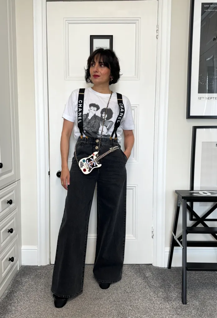 Laura Gallo-Wallis wearing a white Chanel t-shirt with black suspenders, black wide-leg jeans, and a guitar-shaped handbag.