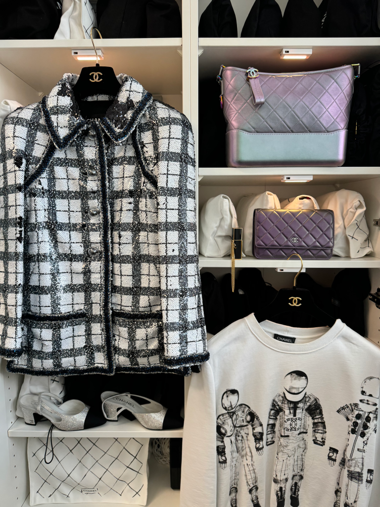 A white closet filled with Chanel clothing, including a sequined plaid jacket, quilted handbags, and shoes.