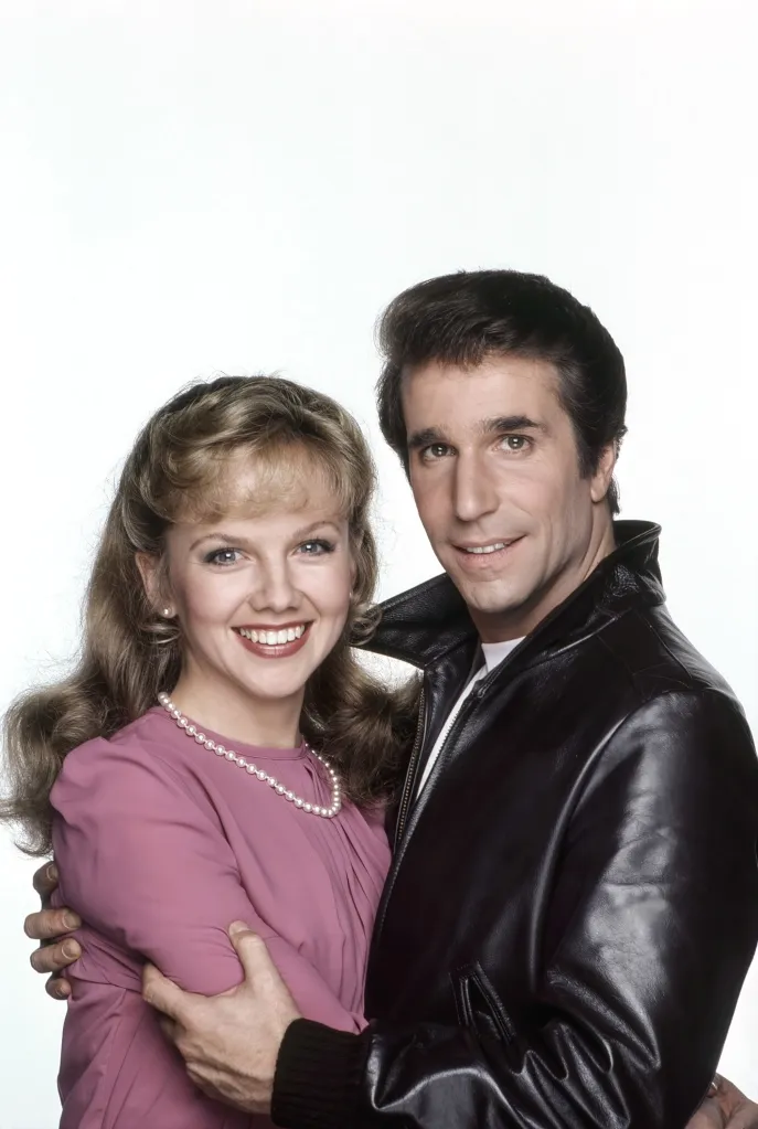 Linda Purl and Henry Winkler smiling, with Winkler wearing a leather jacket and Purl in a pink dress and pearl necklace.