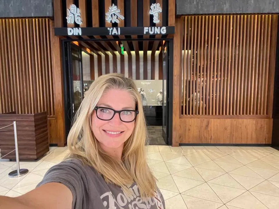 Lindsay Hansen posing for a selfie in front of a Din Tai Fung restaurant.