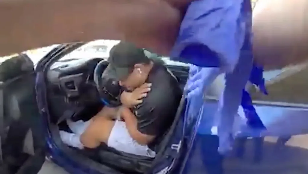Venezuelan migrant Wilber Rafael Garces sits in the seat of his car holding his shoulder as Austin Police respond to the scene of a shooting.