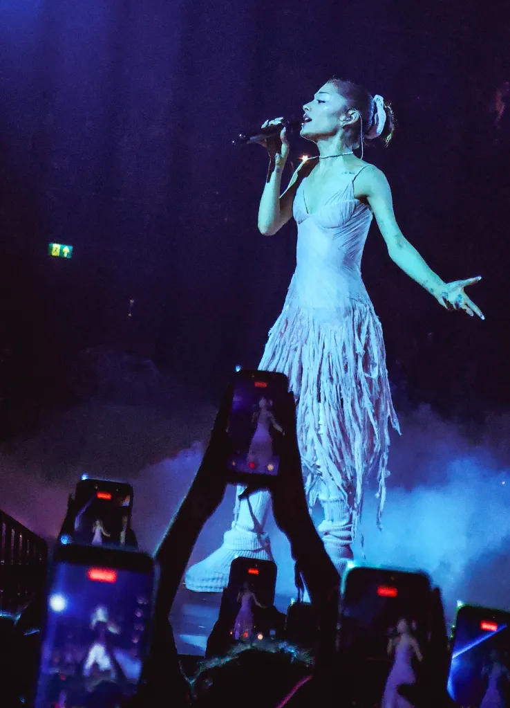 Ariana Grande performing on stage in a white gown at her final London tour show.