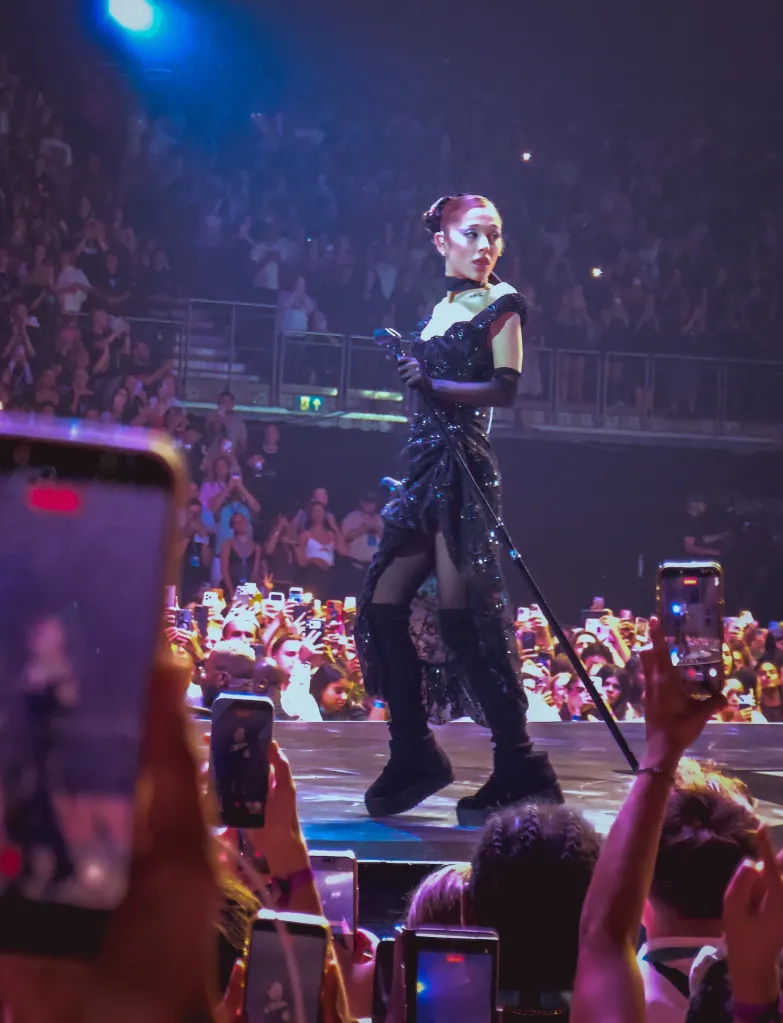 Ariana Grande performing on stage in a black gown at her final London tour show.