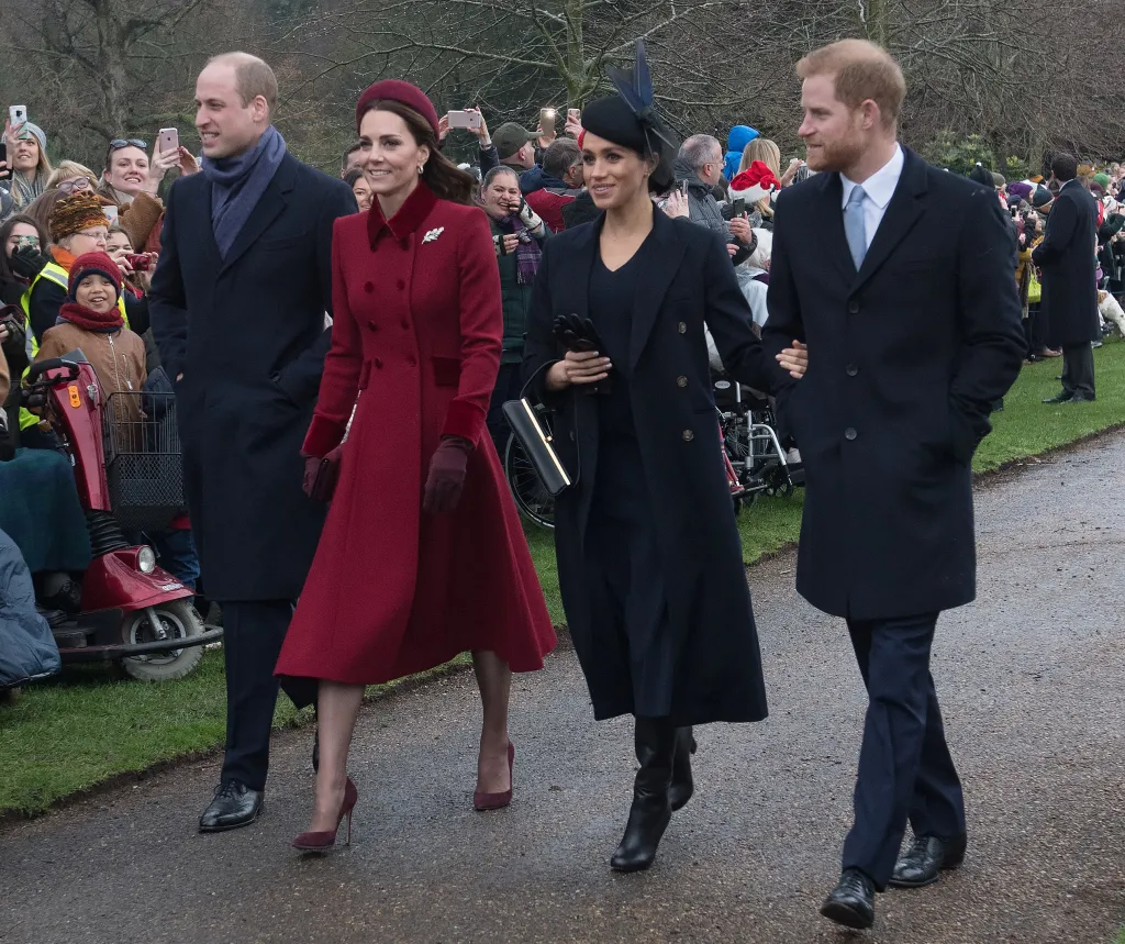 Prince William, Princess Catherine, Meghan Markle, and Prince Harry walk together while being photographed by a crowd.