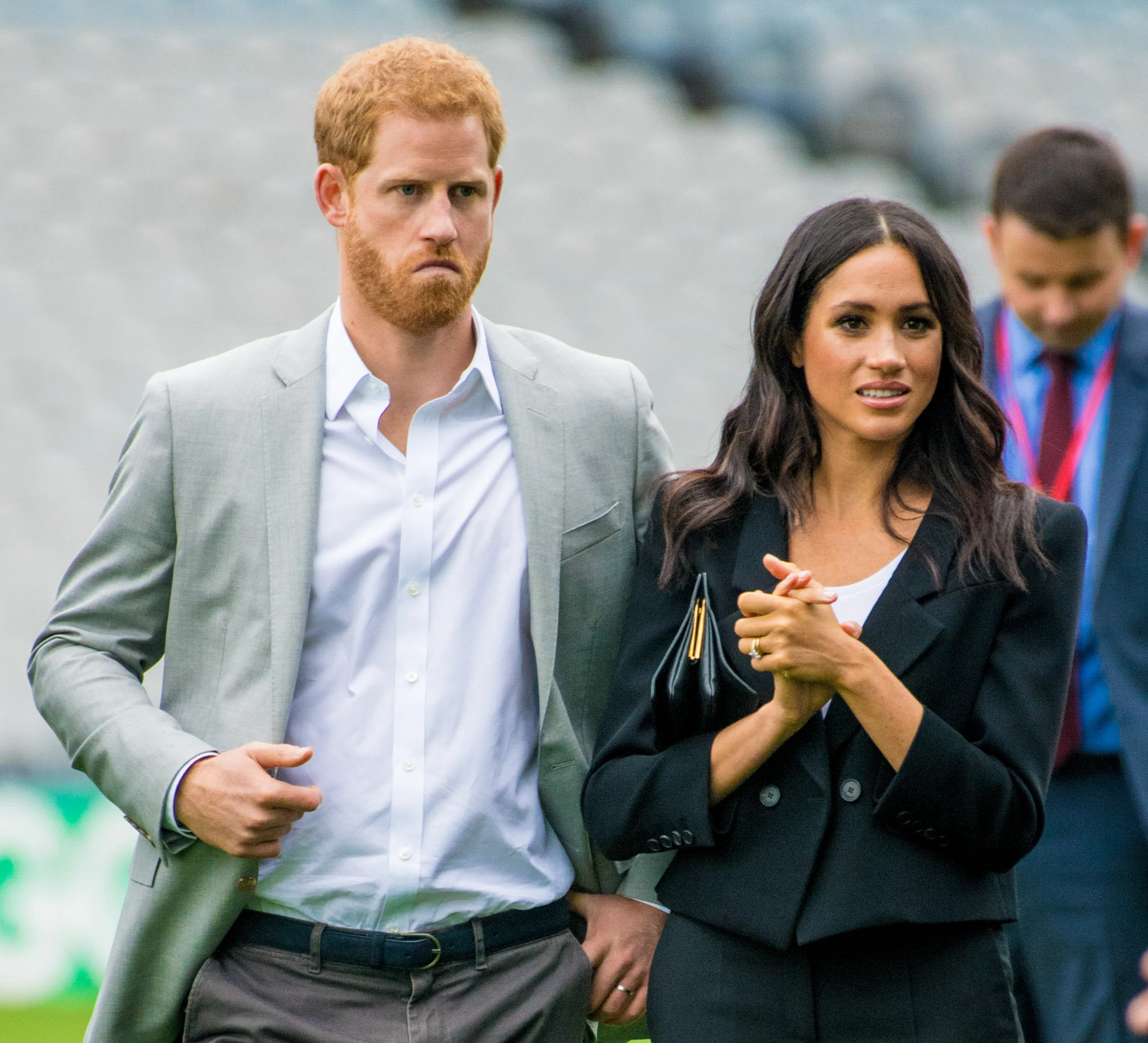Prince Harry and Meghan Markle walking together, with Prince Harry looking forward and Meghan Markle looking to the side.