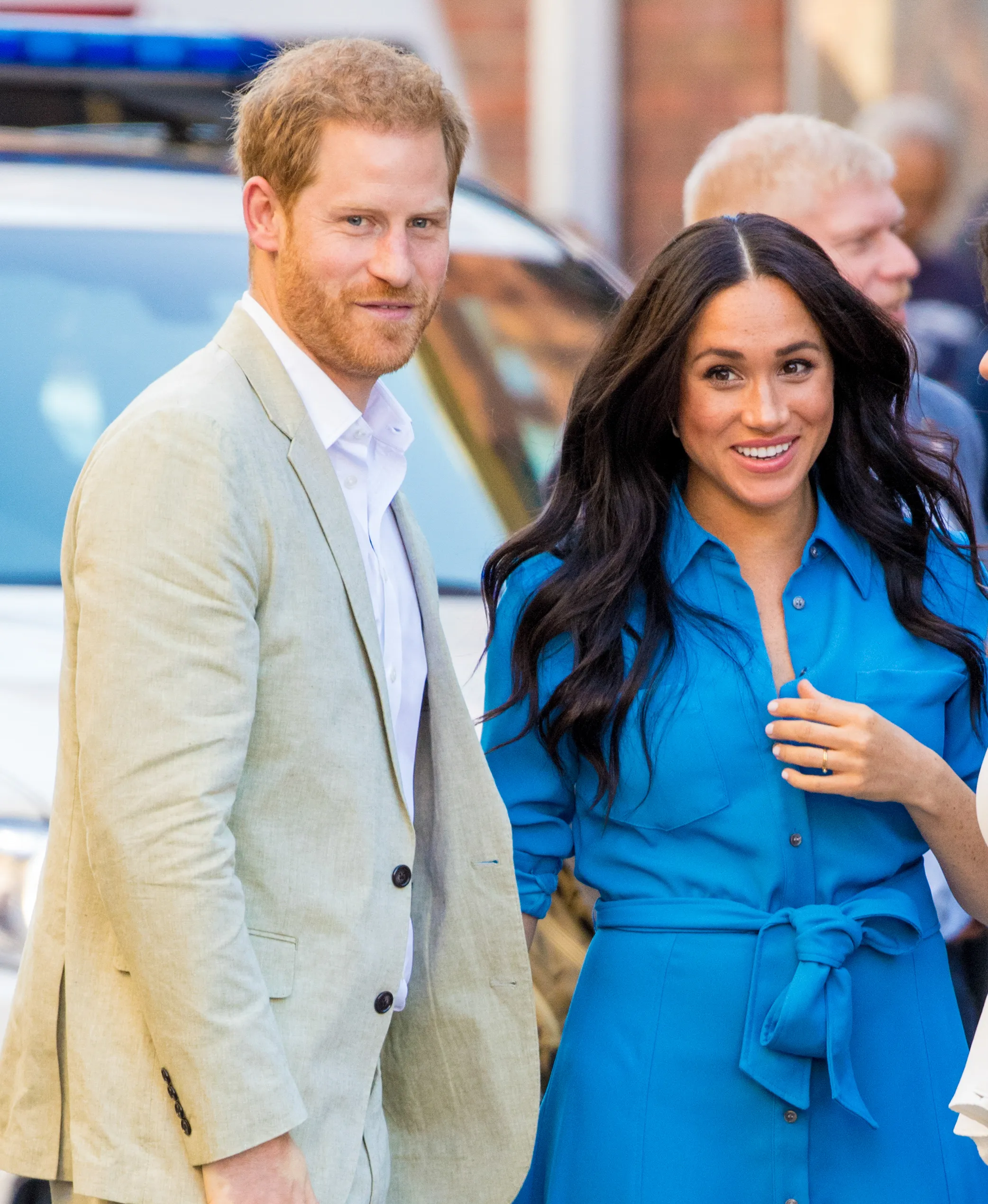 Prince Harry in a light-colored suit jacket and Meghan Markle in a blue dress.