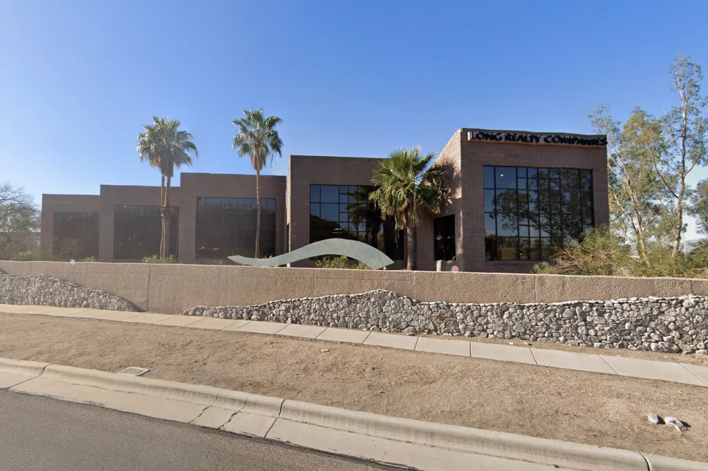 The Long Realty Companies building, featuring palm trees and a low stone wall along the front.