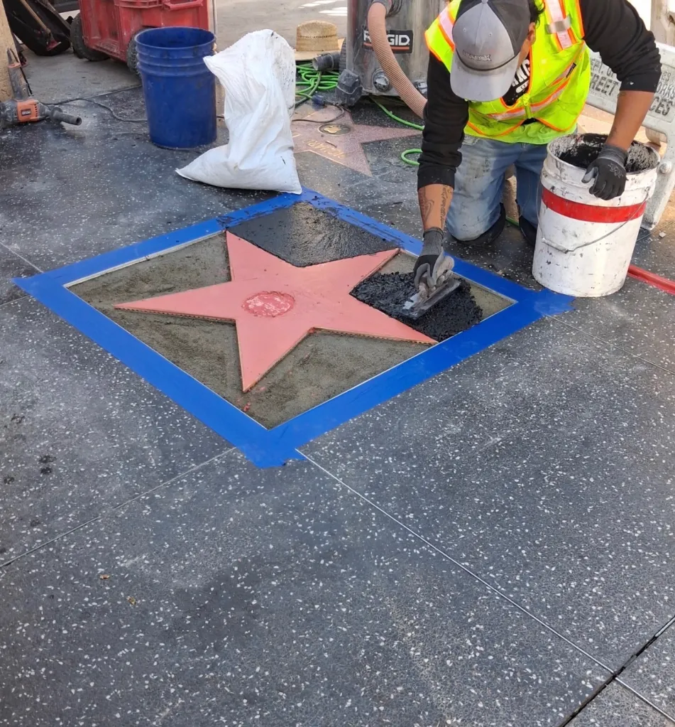A worker restoring Dolly Parton's Hollywood Walk of Fame star, filling the star's points with dark aggregate.