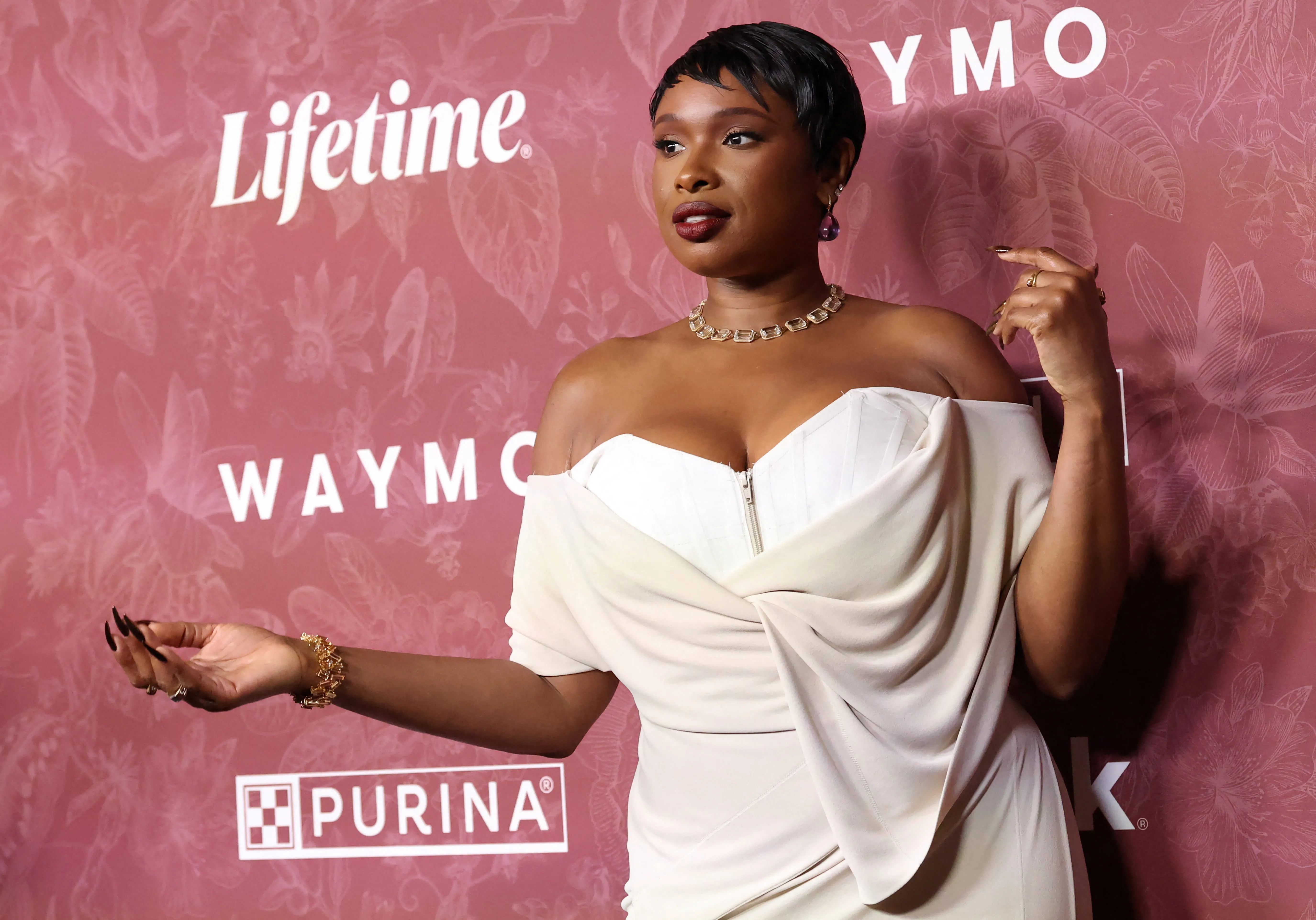 Jennifer Hudson wearing a light-colored off-the-shoulder dress with a visible corset top and a gold necklace.
