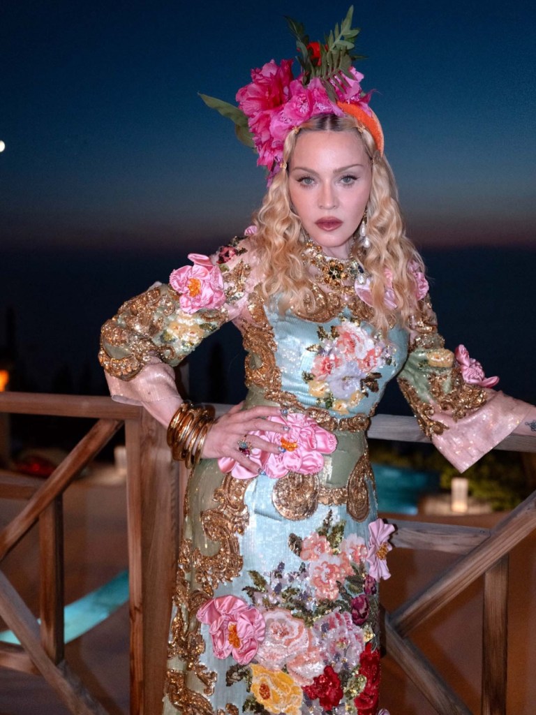 Madonna wearing an elaborate floral dress and headpiece, with the moon visible in the night sky behind her.