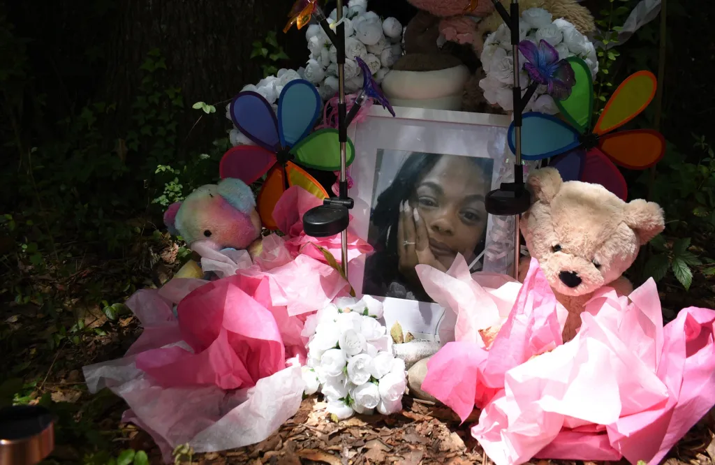 A makeshift memorial for Tasia Fortune including a framed photo, flowers, pinwheels, and teddy bears.