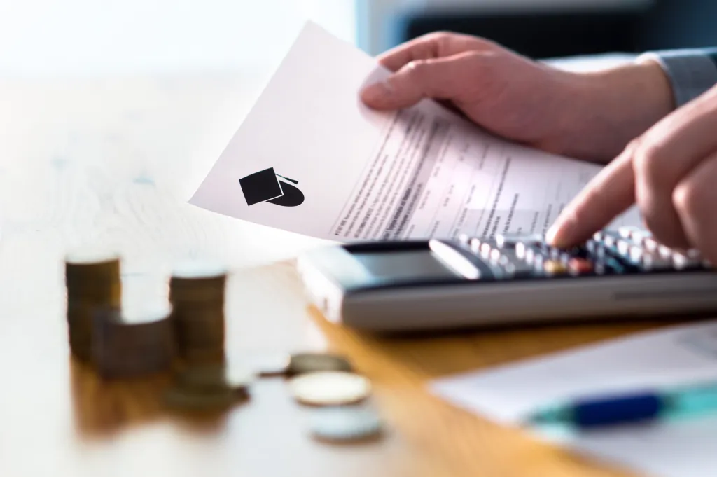 A person using a calculator to figure out college costs, with a document showing a graduation cap icon.