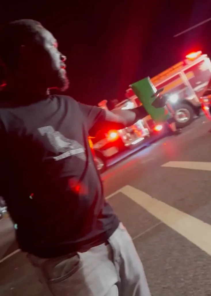 Man retrieves his DoorDash order from the scene of a car accident at night, with a fire truck in the background.