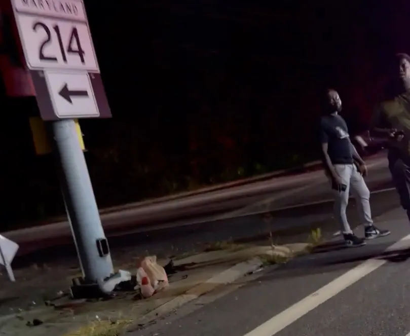Man picking up a DoorDash order next to a broken sign on the side of the road at night.