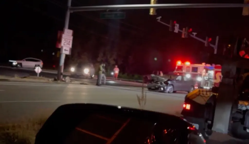 A car crash at night with emergency vehicles, a tow truck, and people standing near the damaged vehicles.