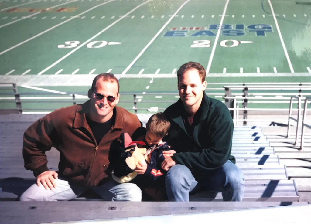 Marco Greenberg and Danny Lewin with a child at a football stadium.