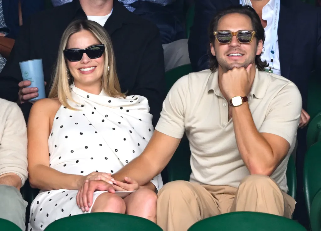 Margot Robbie and Tom Ackerley smiling while seated at Wimbledon.