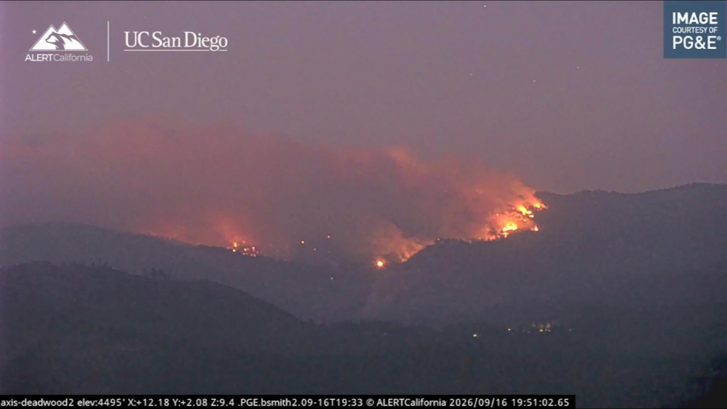 Wildfire burning across forested mountain ridges.
