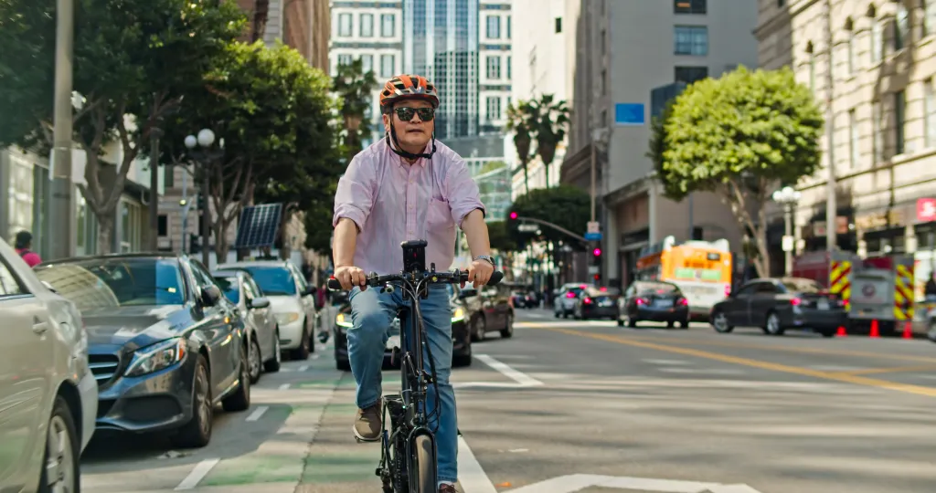 A mature Asian man in his 60s riding a folding bike in a bike lane in downtown Los Angeles.