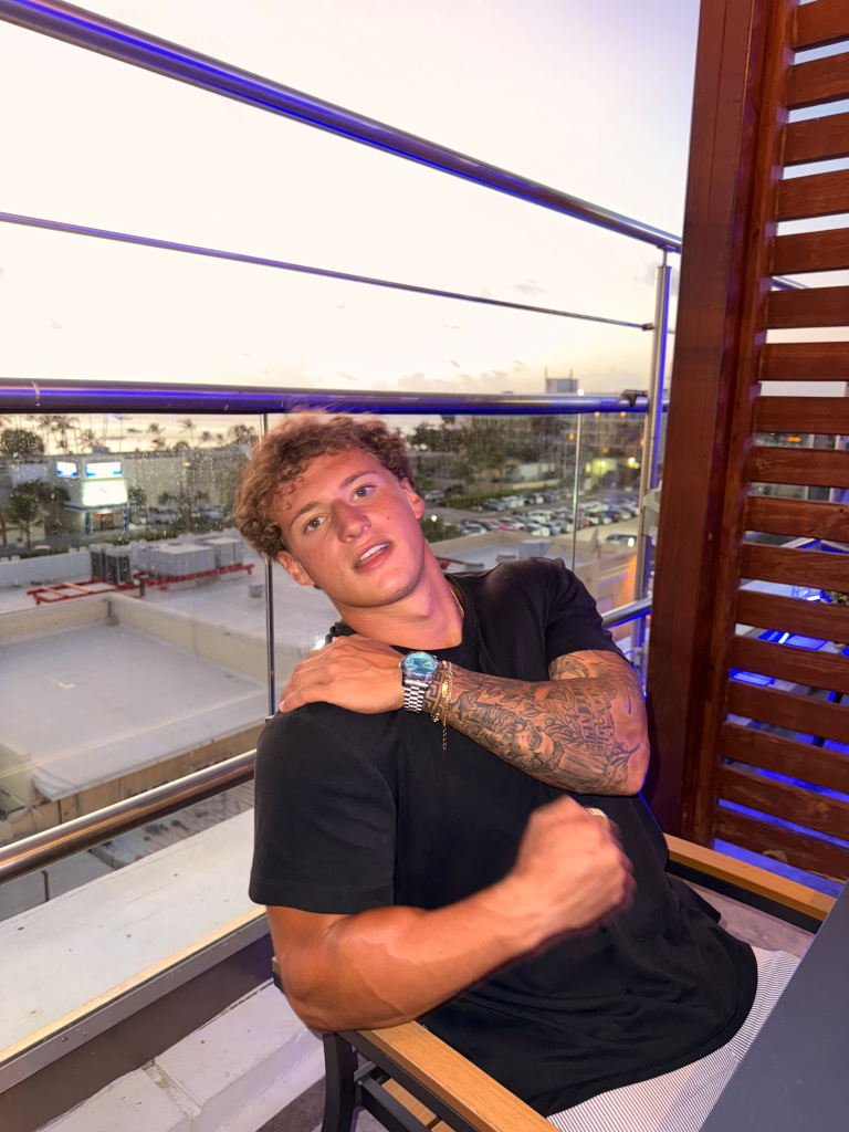 Max Rodman, CEO at Kalos, poses for a photo on a balcony overlooking a city at dusk.