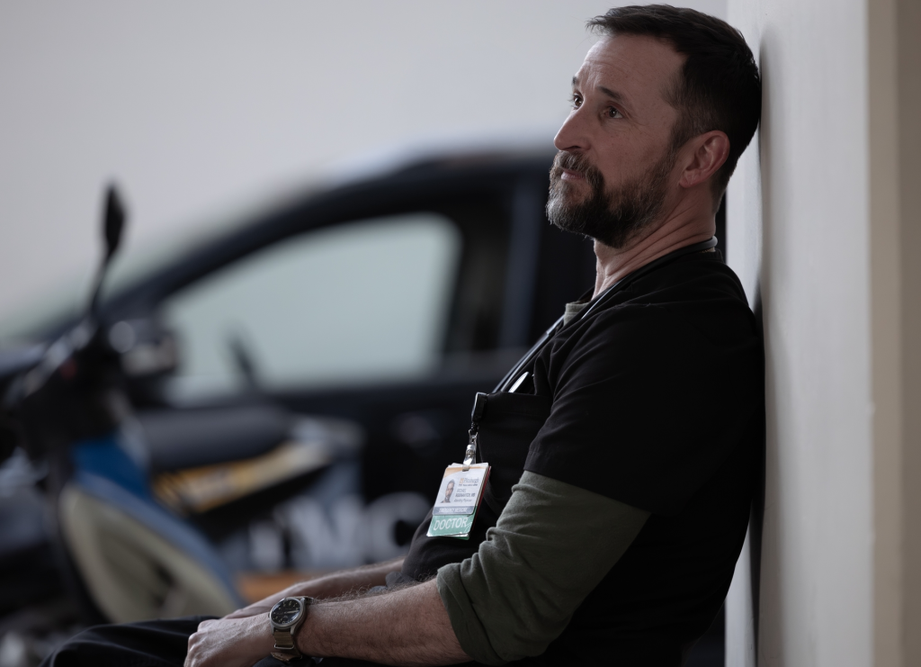 Noah Wyle as Dr. Robby Rubinovitch, looking up while leaning against a wall.