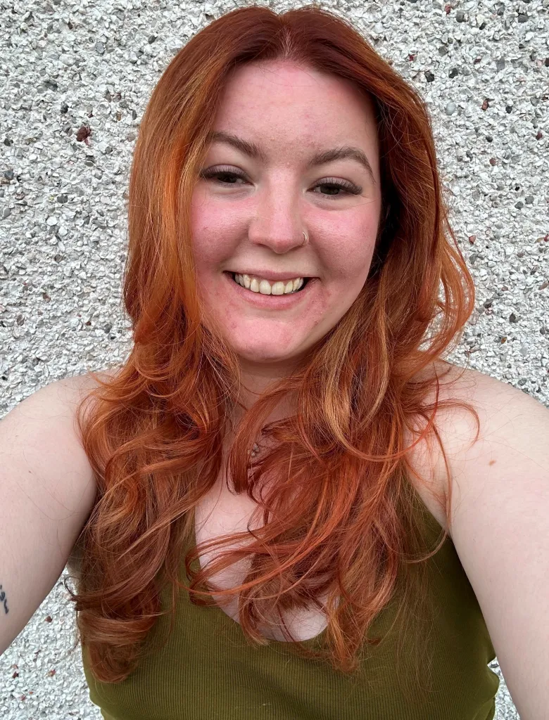 Megan Wright smiling, wearing a green top, with long red hair against a textured wall.