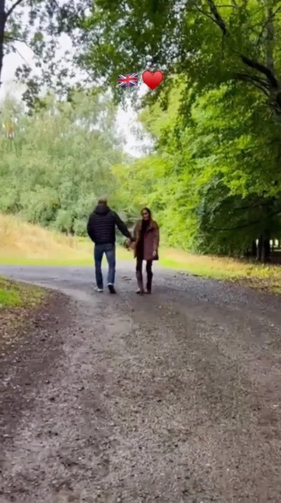 Meghan Markle and Prince Harry holding hands while walking down a path in a park, with emojis of a Union Jack and a heart above them.