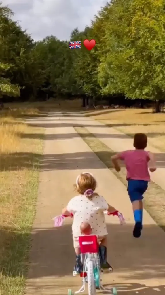 A boy running next to a girl on a tricycle on a long driveway.