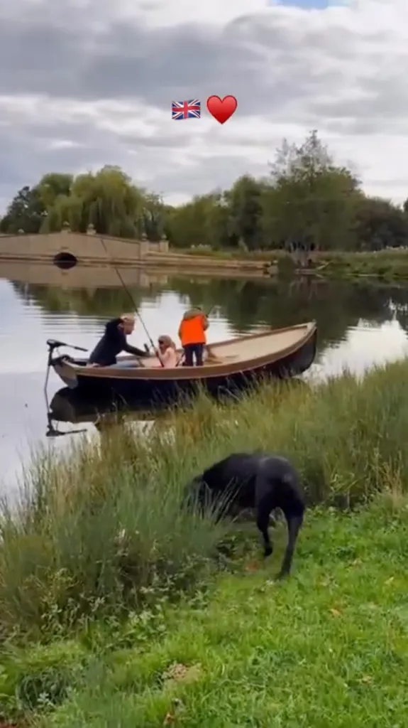 Meghan Markle and Prince Harry with a child on a boat, with a dog on the grassy bank.