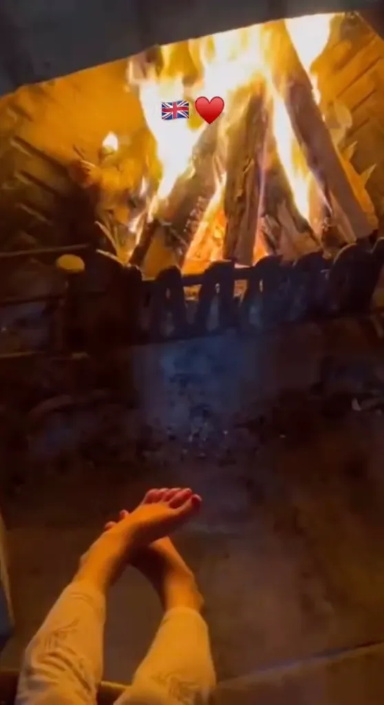 A person's feet resting in front of a fireplace with a Union Jack flag and a red heart emoji.