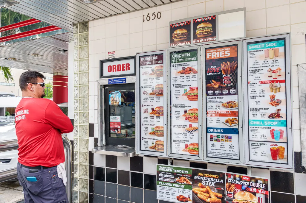 A man in a red shirt reads the menu at a Checkers drive-thru window.