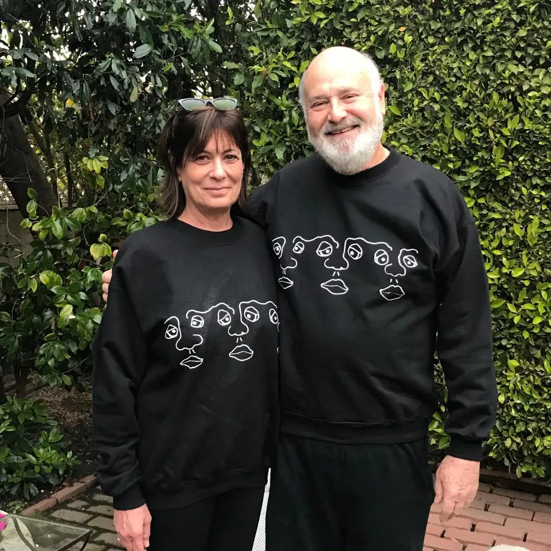 Rob and Michele Reiner in matching black sweatshirts with white line art faces.