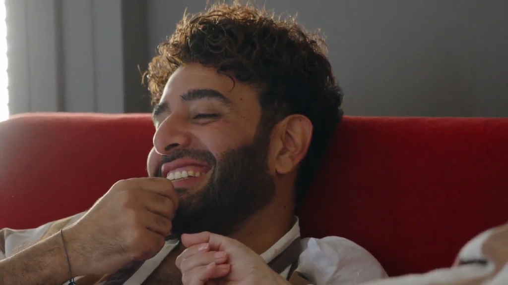 Mido laughing with his eyes closed while wearing a white shirt with red stripes.