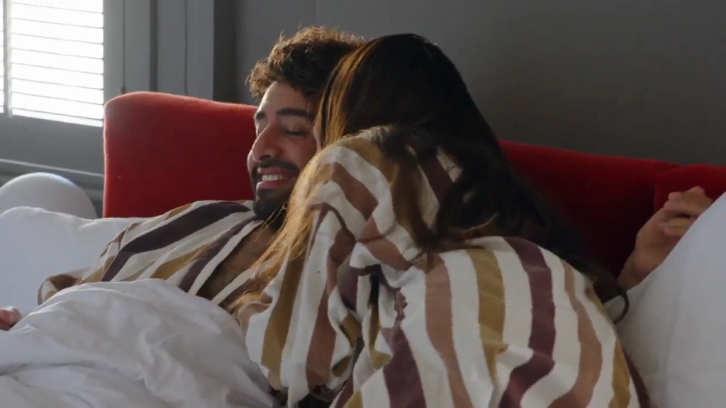 A man with a beard and a woman with long dark hair lying in bed together.