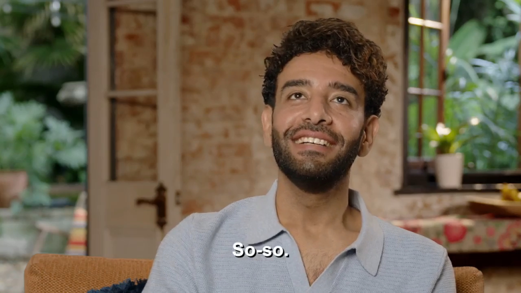 Mido, a man with a beard and curly hair, smiles while looking up.