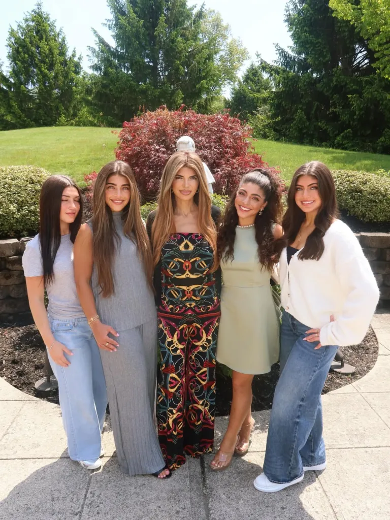Five women standing outdoors, smiling at the camera.