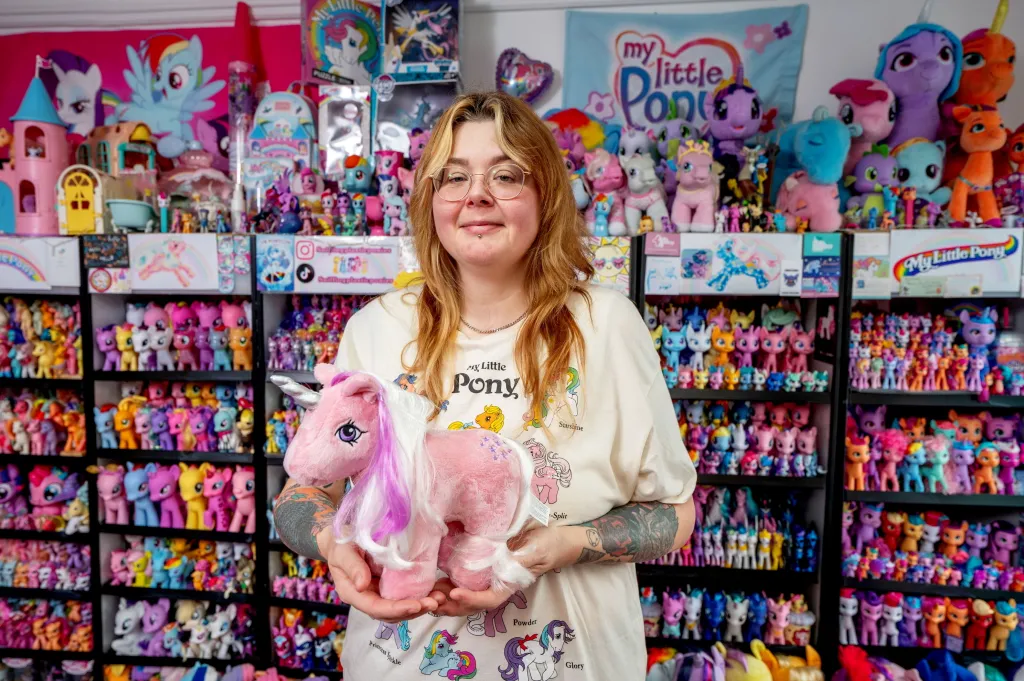 Mirandia Worby holds a pink unicorn plushie in front of her massive My Little Pony collection.