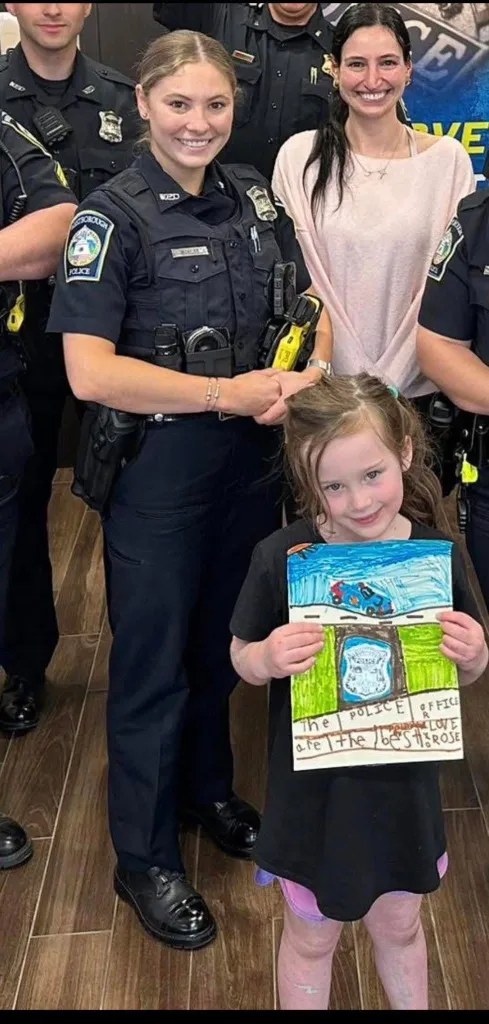 Ashlyn Mercier in her police uniform, smiling next to a child holding a drawing that says