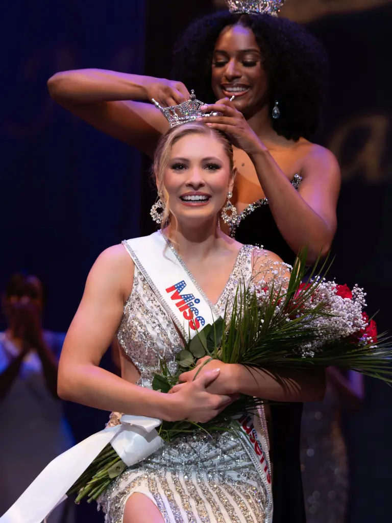 Ashlyn Mercier smiling as a woman places a crown on her head.