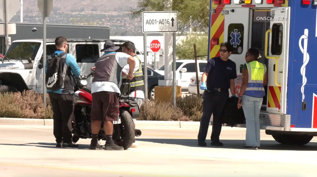 People gathered around a red motorcycle next to an ambulance and a stop sign outside an Amazon warehouse.