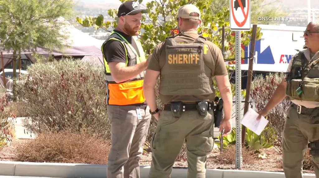A man in a reflective vest speaking with a sheriff's deputy in front of an Amazon warehouse.