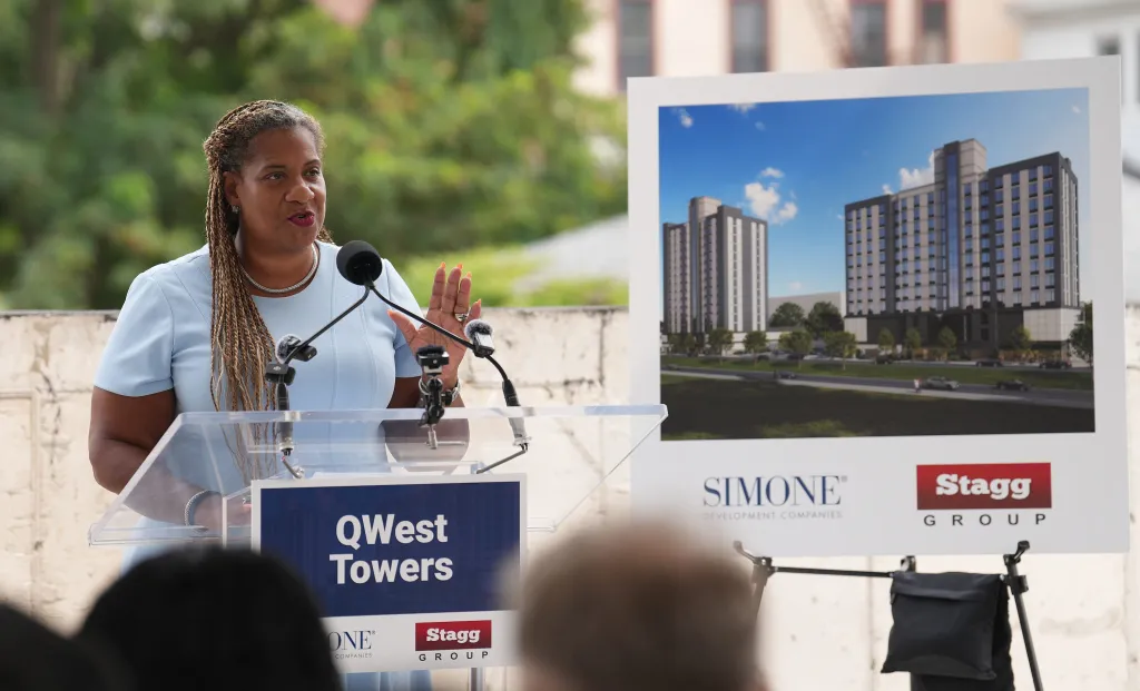 Mount Vernon Mayor Shawyn Patterson-Howard speaking at a podium with a QWest Towers rendering in the background.