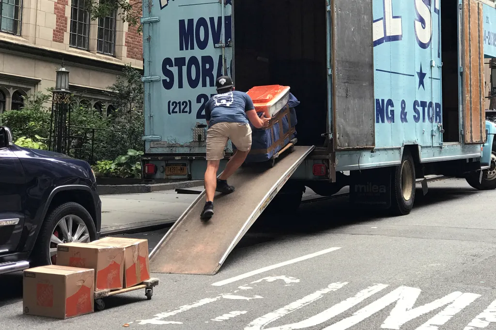 A mover pushes a large item up a ramp into the back of a blue moving truck.