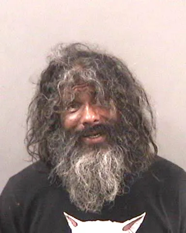 Mugshot of Kenneth Stine, a man with long, dark, curly hair and a graying beard, wearing a dark t-shirt.