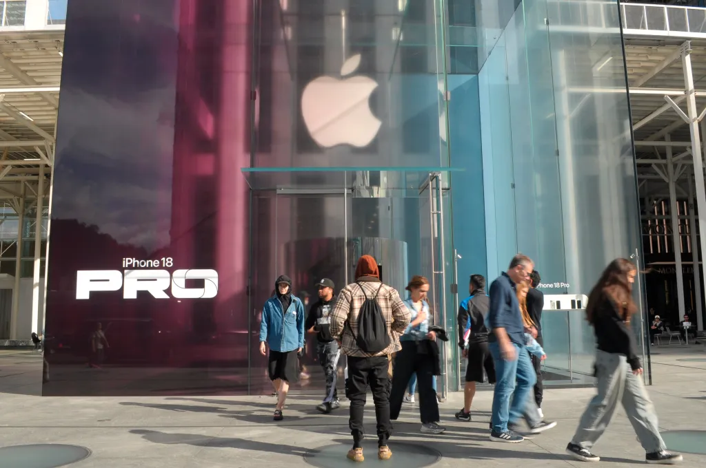 The iPhone 18 Pro is advertised on the glass facade of the Apple store on Fifth Avenue in Manhattan, with pedestrians walking in front.